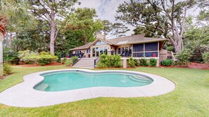 A house with a swimming pool, a deck, and a large tree in the backyard.