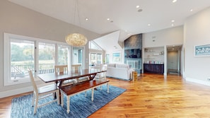 A spacious living area with a wooden dining table, white sofas, and a large window overlooking a garden.