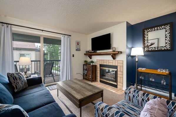 A living room with a fireplace, a television, and a balcony with a view of the outside.