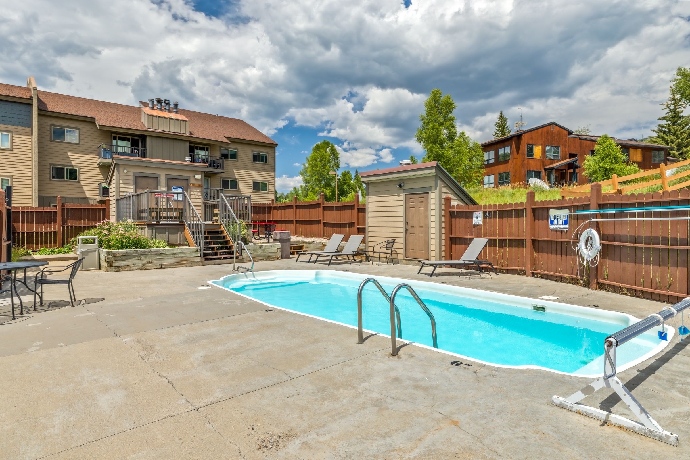 A residential area with a swimming pool, outdoor furniture, and a wooden fence.