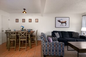 A living room with a dark sofa, patterned armchair, and a dining area with wooden chairs and a table.