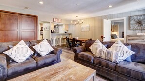 A living room with leather sofas, wooden coffee table, and a dining area with a kitchen in the background.