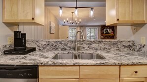 A kitchen with wooden cabinets, a granite countertop, a stainless steel sink, a coffee maker, and a dishwasher.