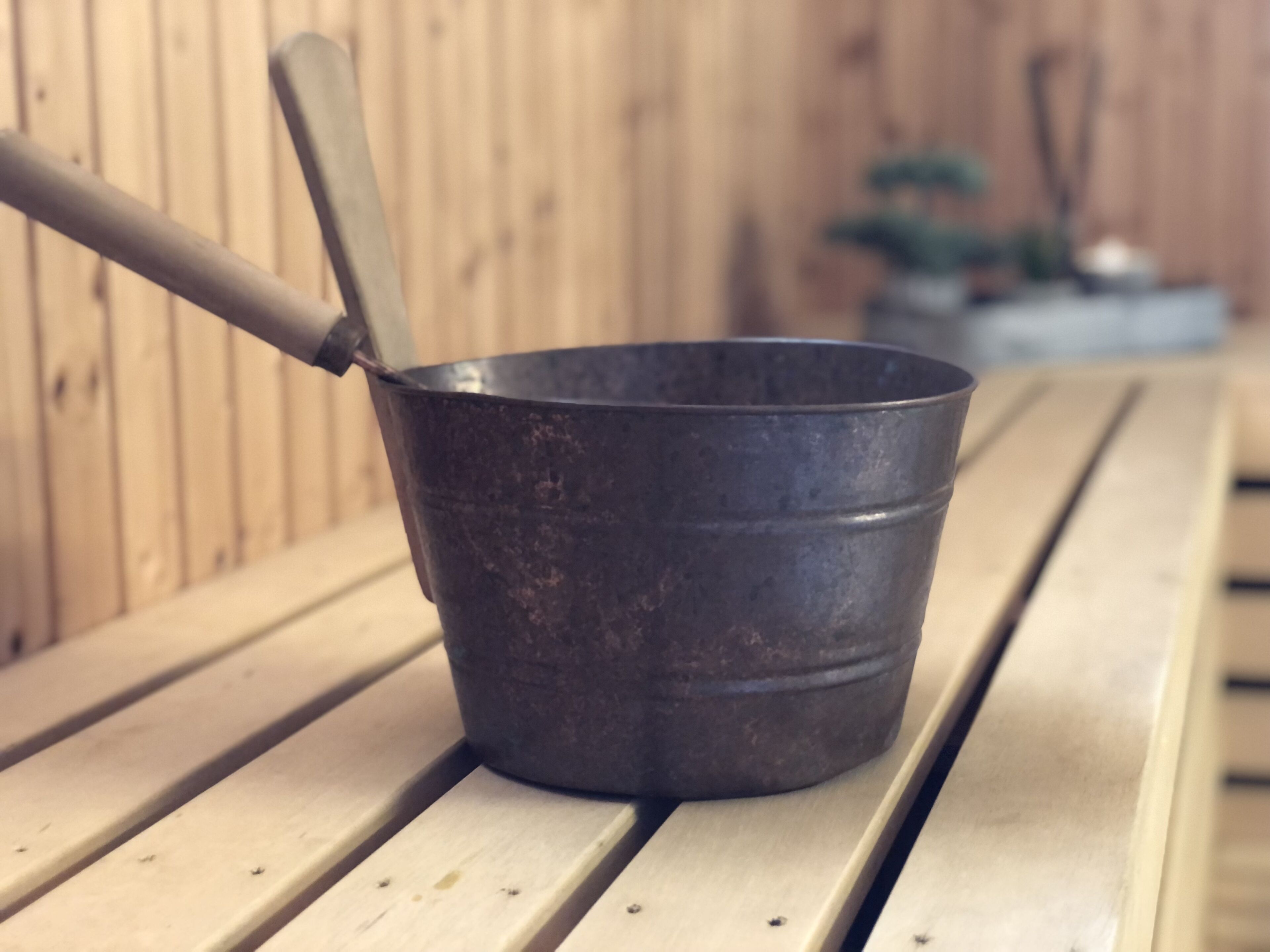 A metal bucket with a handle on a wooden bench.