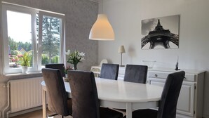 Moderni ruokailutila, jossa on valkoinen pöytä ja tummat tuolit, riippuvalaisin, kannettava tietokone ja seinällä oleva kehystetty kuva Eiffel-tornista.