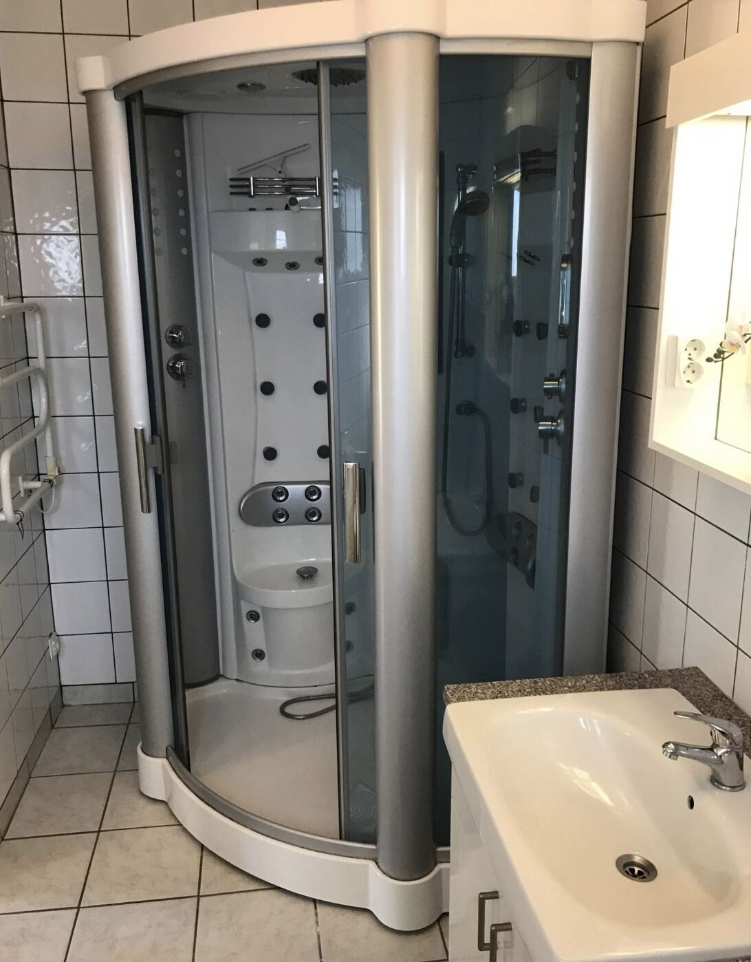 A modern bathroom with a glass-enclosed shower, a standalone sink, and tiled walls.