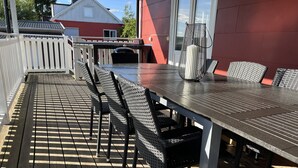 Ulkoterassi, jossa on pitkä pöytä ja useita tuoleja, ja sen ympärillä on valkoinen puinen aita.