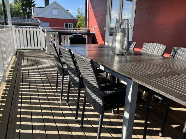 An outdoor patio with a long table and multiple chairs, surrounded by a white picket fence.