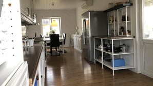 Keittiössä on puulattiat, valkoiset kaapit, sisäänrakennettu jääkaappi sekä ruokailutila, jossa on pöytä ja tuolit.