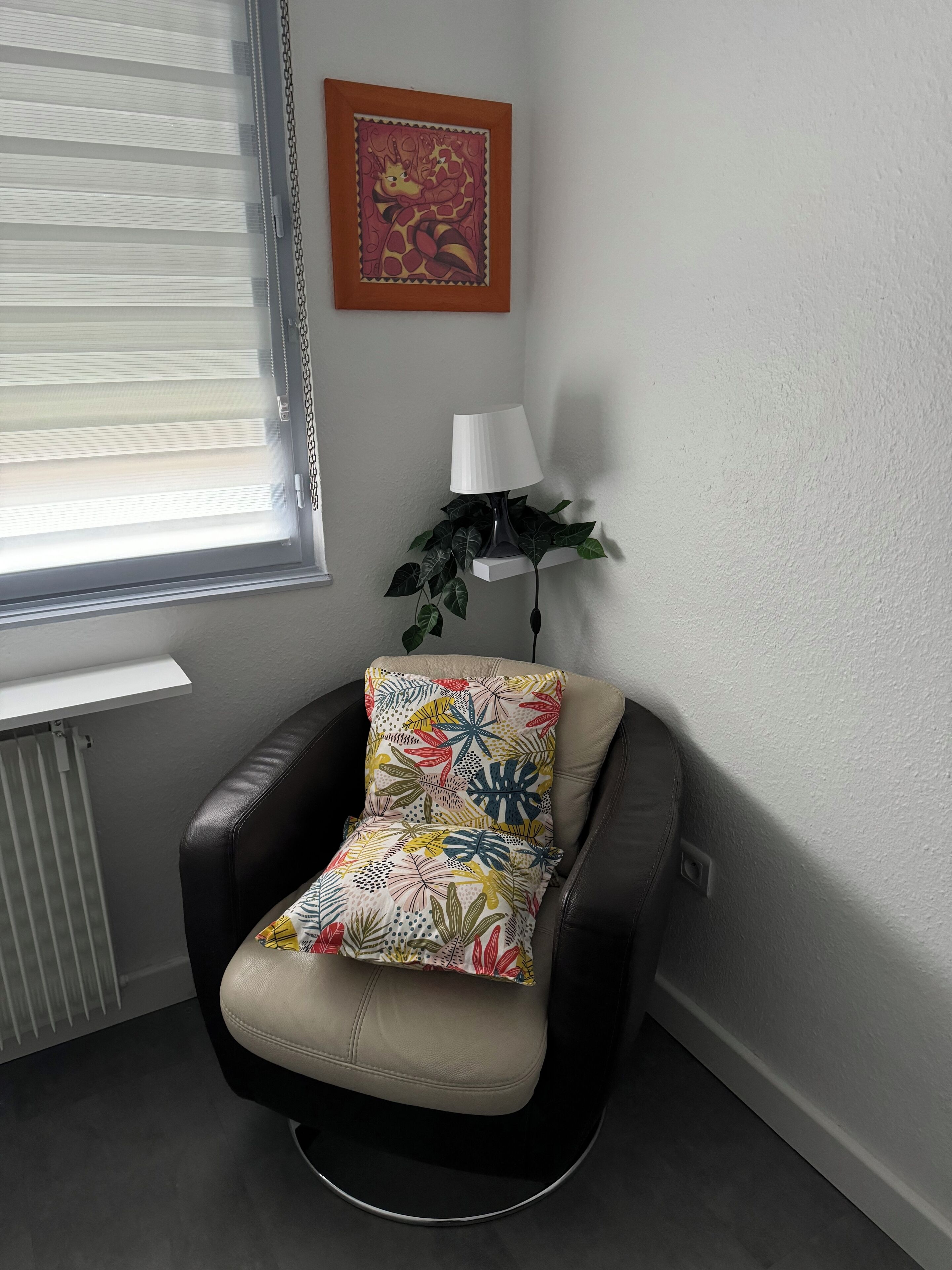 A modern chair with a floral cushion, a white lamp, and a framed artwork on the wall.