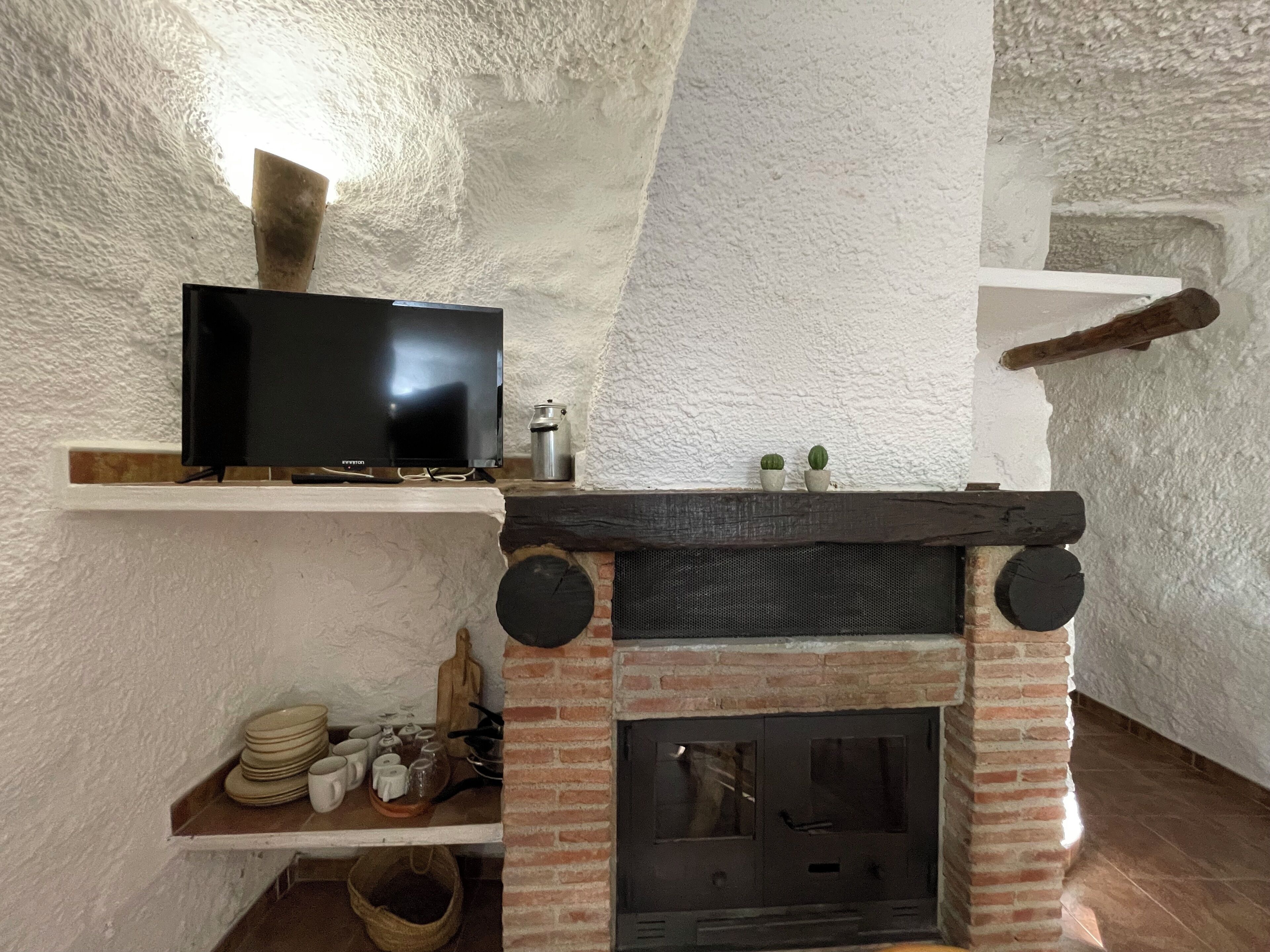 Een gezellige kamer met een open haard, een televisie op een plank, en een rustieke bakstenen muur.