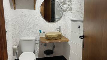 Un baño pequeño con inodoro, lavabo de encimera de madera, espejo y un estante con artículos de aseo.