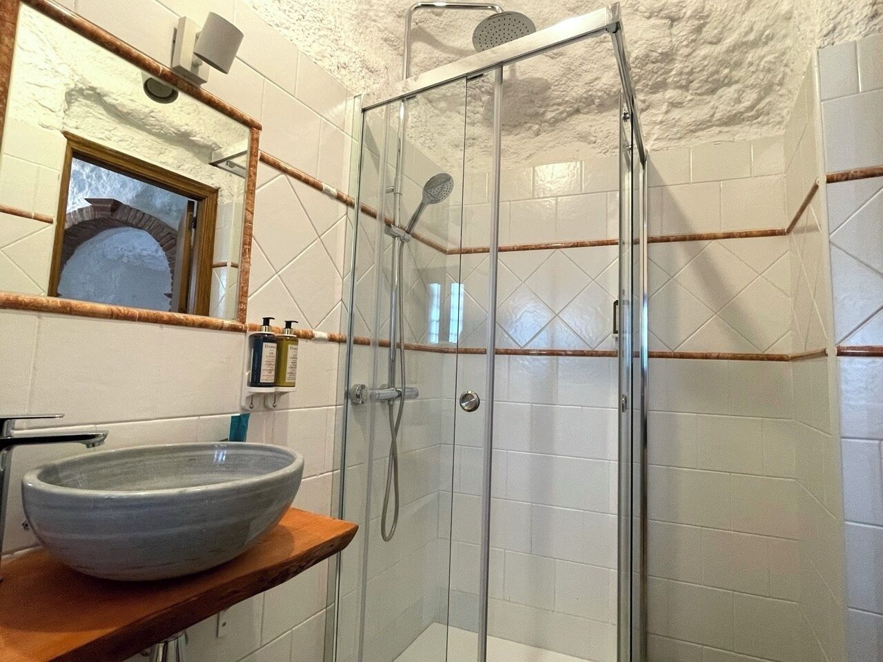 Un baño con ducha de vidrio, un lavamanos de cerámica grande y una encimera de madera.