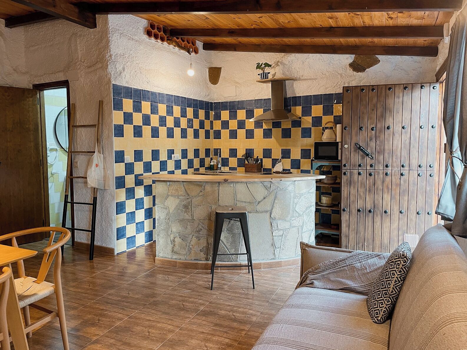 A cozy kitchen with a checkered tile backsplash, a stone island, wooden beams, and a wooden cabinet.