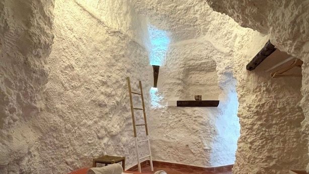 Una habitación acogedora y aislada con una escalera de madera, un estante pequeño y toallas dobladas cuidadosamente sobre un tapete rojo.