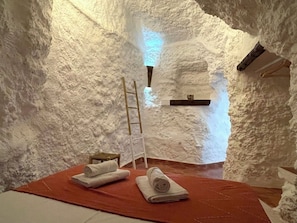 A cozy, insulated room with a wooden ladder, a small shelf, and neatly folded towels on a red mat. - Cuevas El Atochal OrÃgenes (Gor)