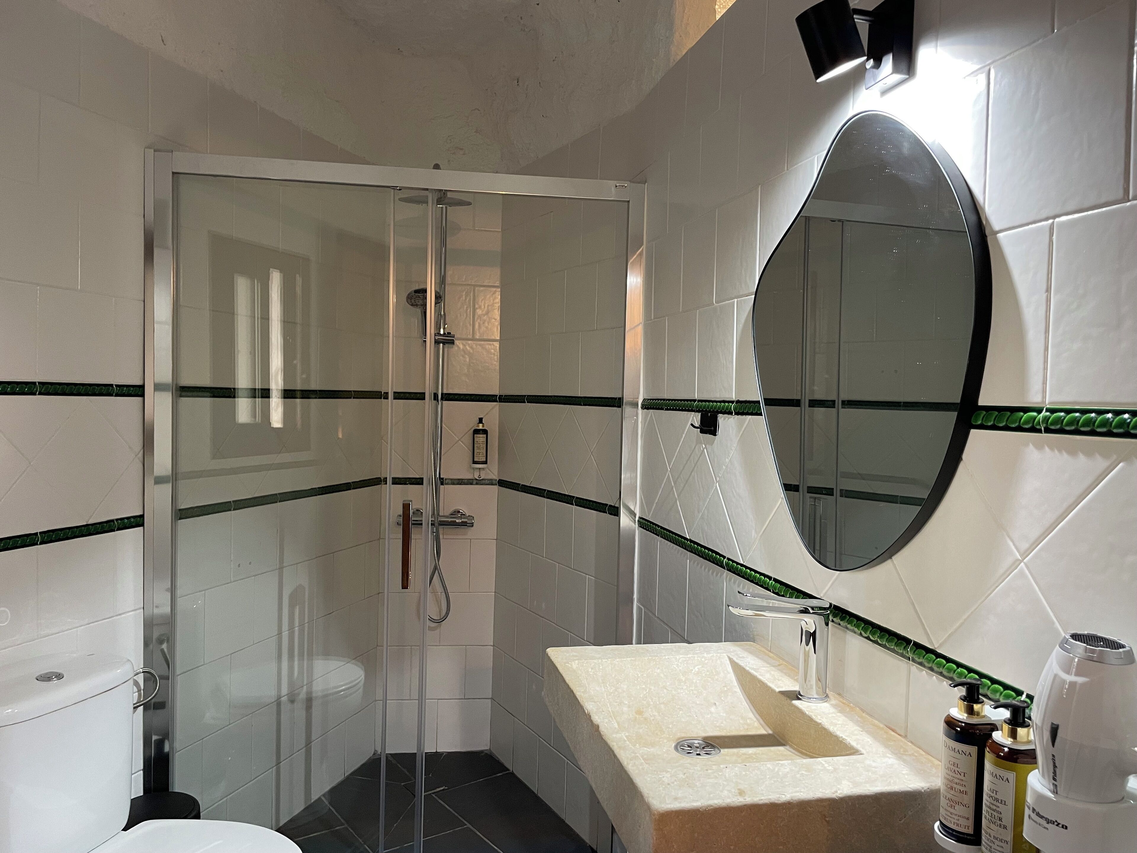 A bathroom with a glass-enclosed shower, a sink with a mirror, and toiletries on the counter.