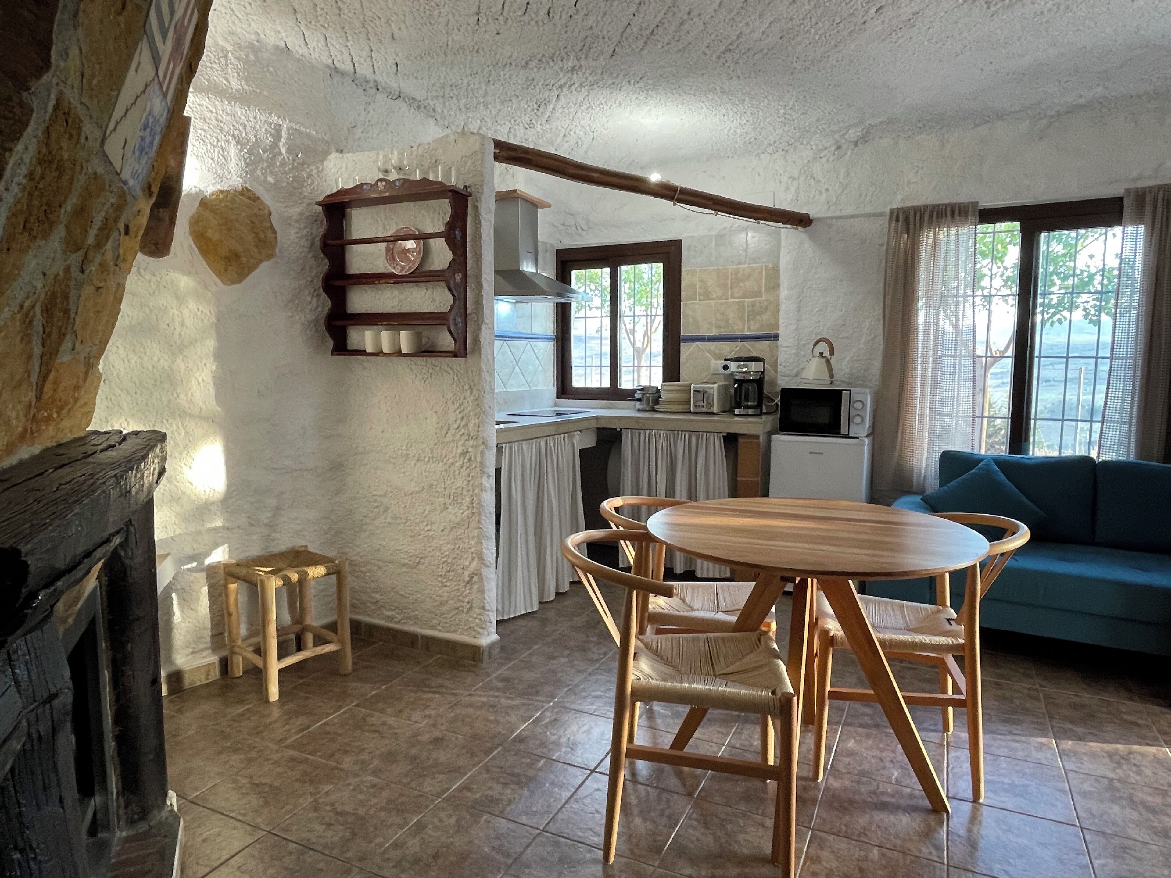 Una sala de estar acogedora con una mesa de comedor de madera y sillas, un sofá, y una zona de cocina con microondas y cafetera.