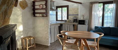 Una sala de estar acogedora con una mesa de comedor de madera y sillas, un sofá, y una zona de cocina con microondas y cafetera.