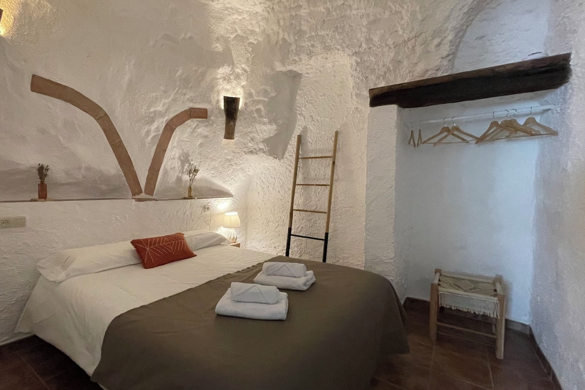A bedroom with a bed, pillows, a bedside table with a lamp, a wooden ladder, and a clothing rack.