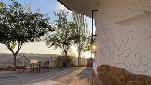 Un patio al aire libre con muros de piedra, una zona de estar con sillas y una mesa, y vistas del paisaje.