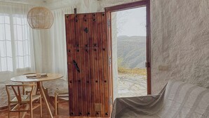 Una habitación rústica con una puerta de madera, una mesa redonda con sillas, un sofá y vistas a un paisaje nevado a través de la puerta.