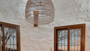 Una mesa de madera redonda con sillas tejidas, una lámpara de techo trenzada y vistas a través de amplias ventanas.