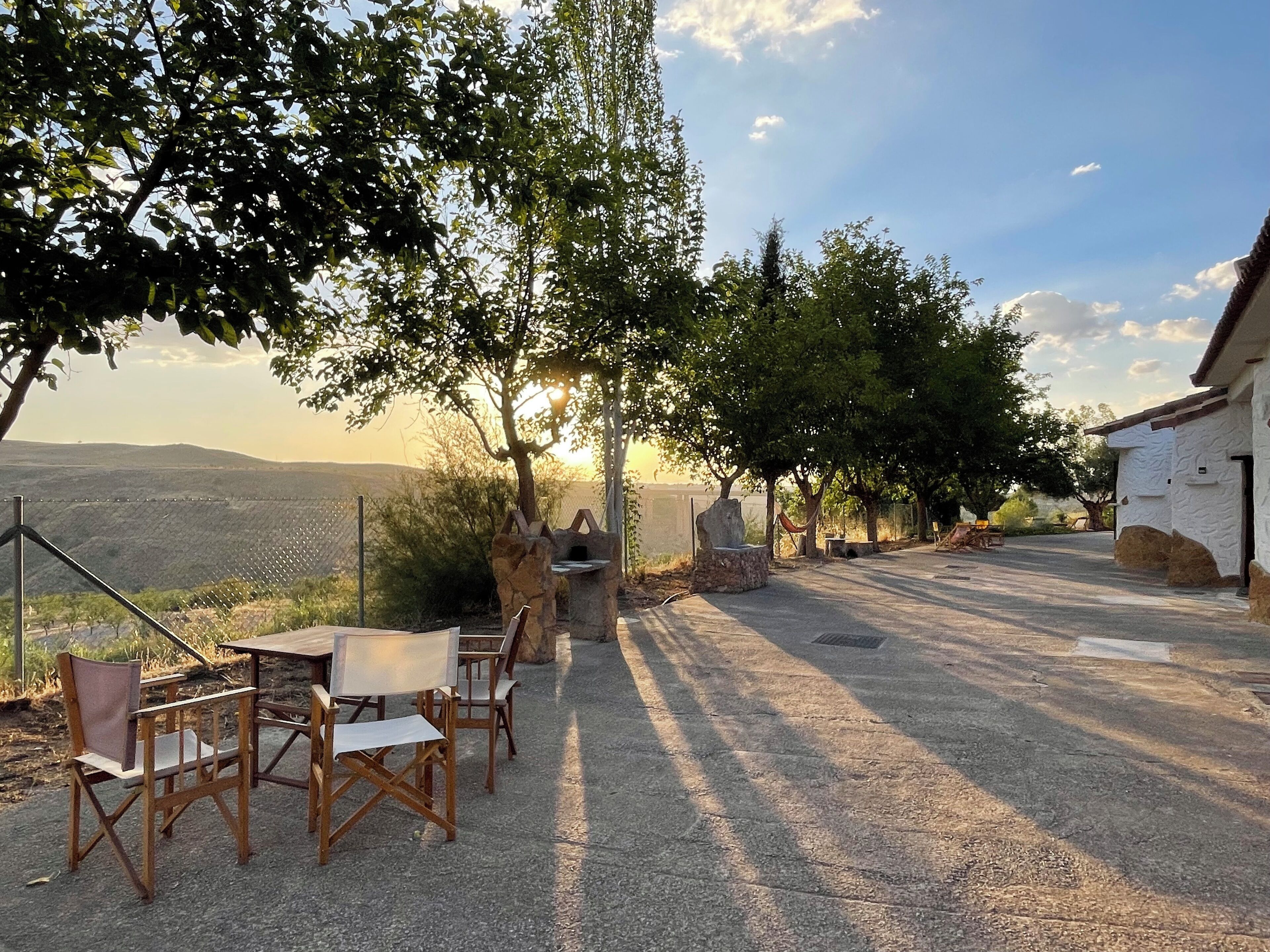 An outdoor seating area with tables and chairs, a stone barbecue, and a view of the surrounding landscape.