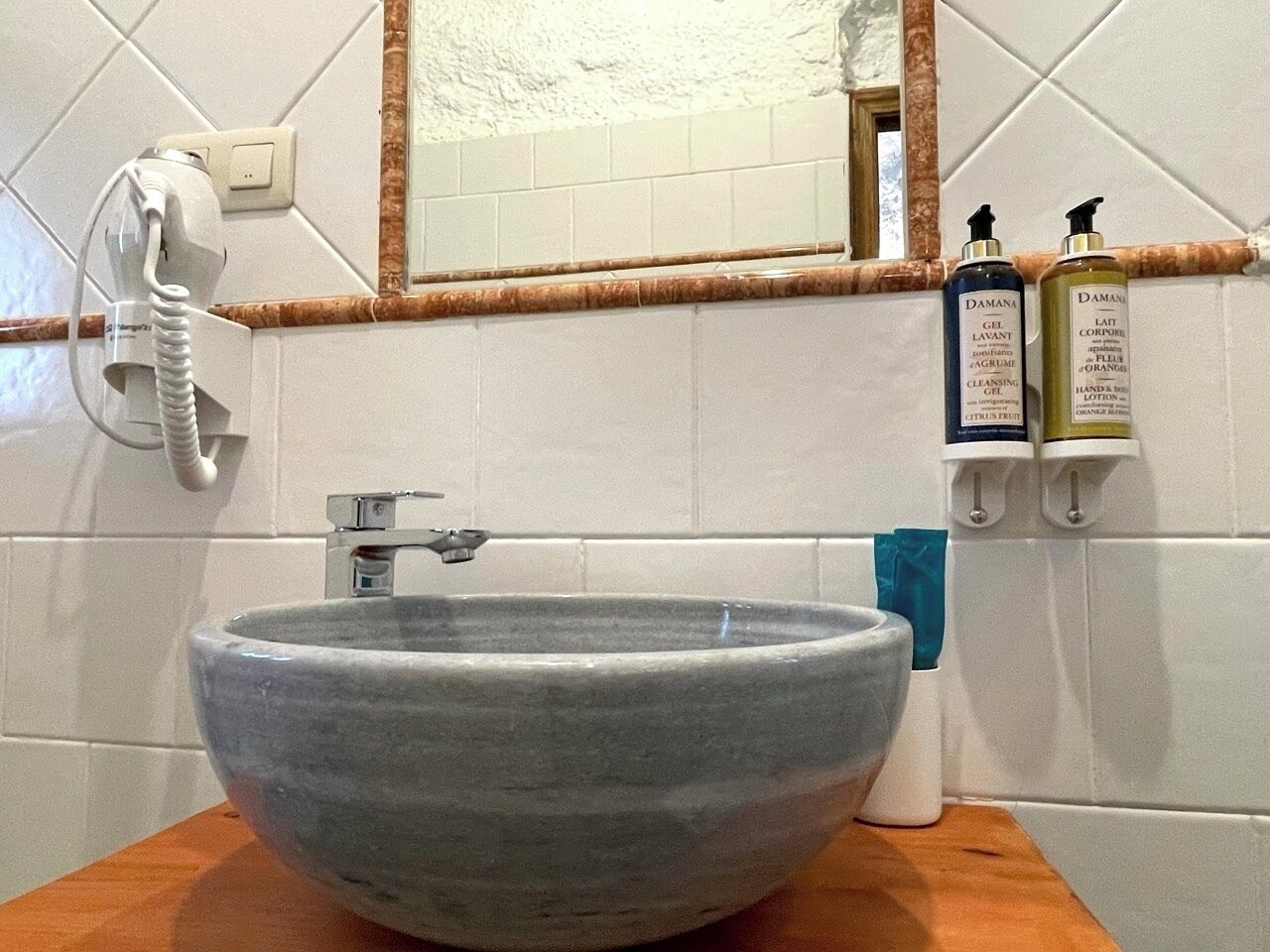 A bathroom with a large ceramic sink, a mirror, and toiletries on a shelf.