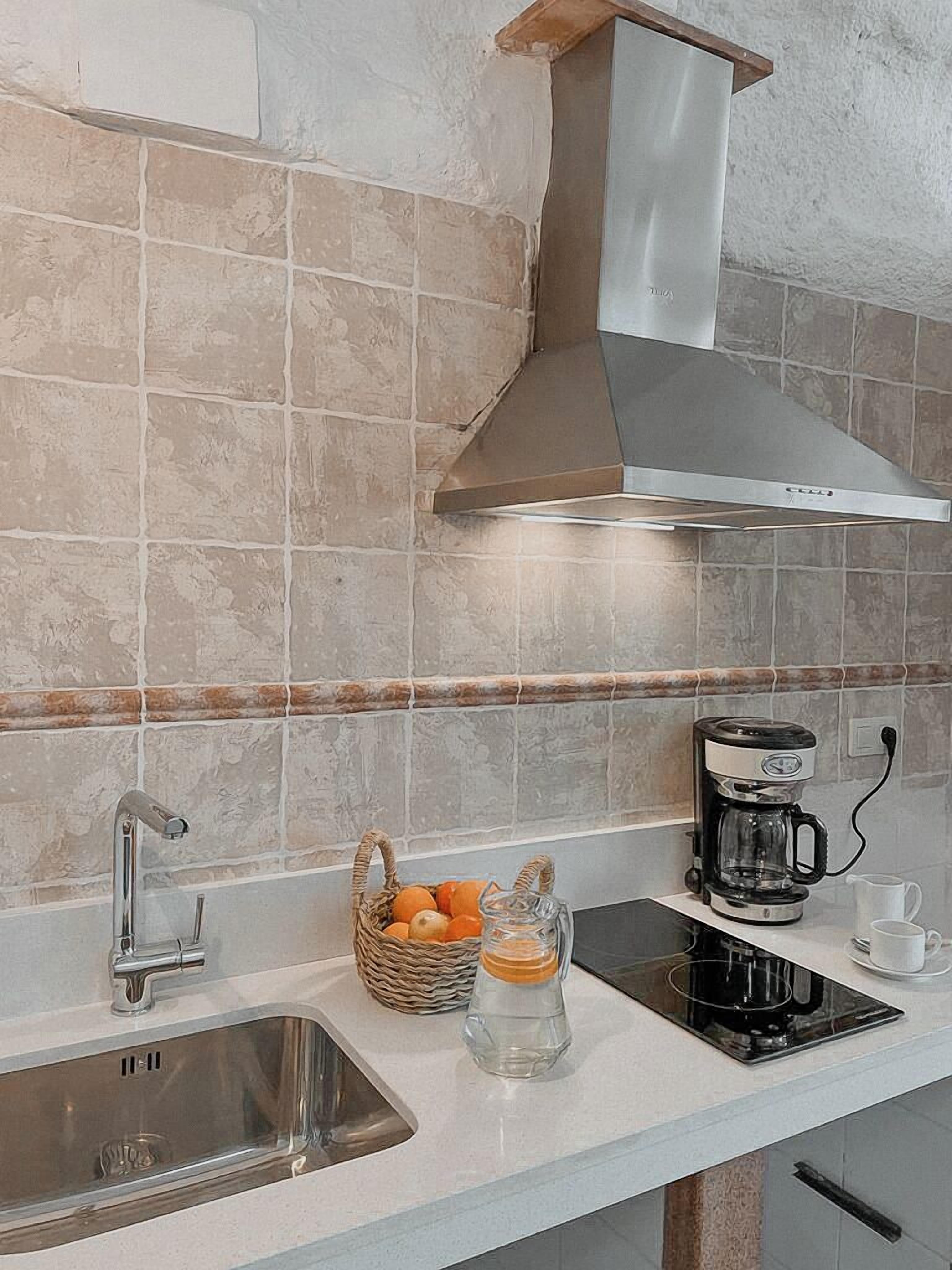 A kitchen with a stainless steel sink, a coffee maker, and a basket of oranges on the counter.
