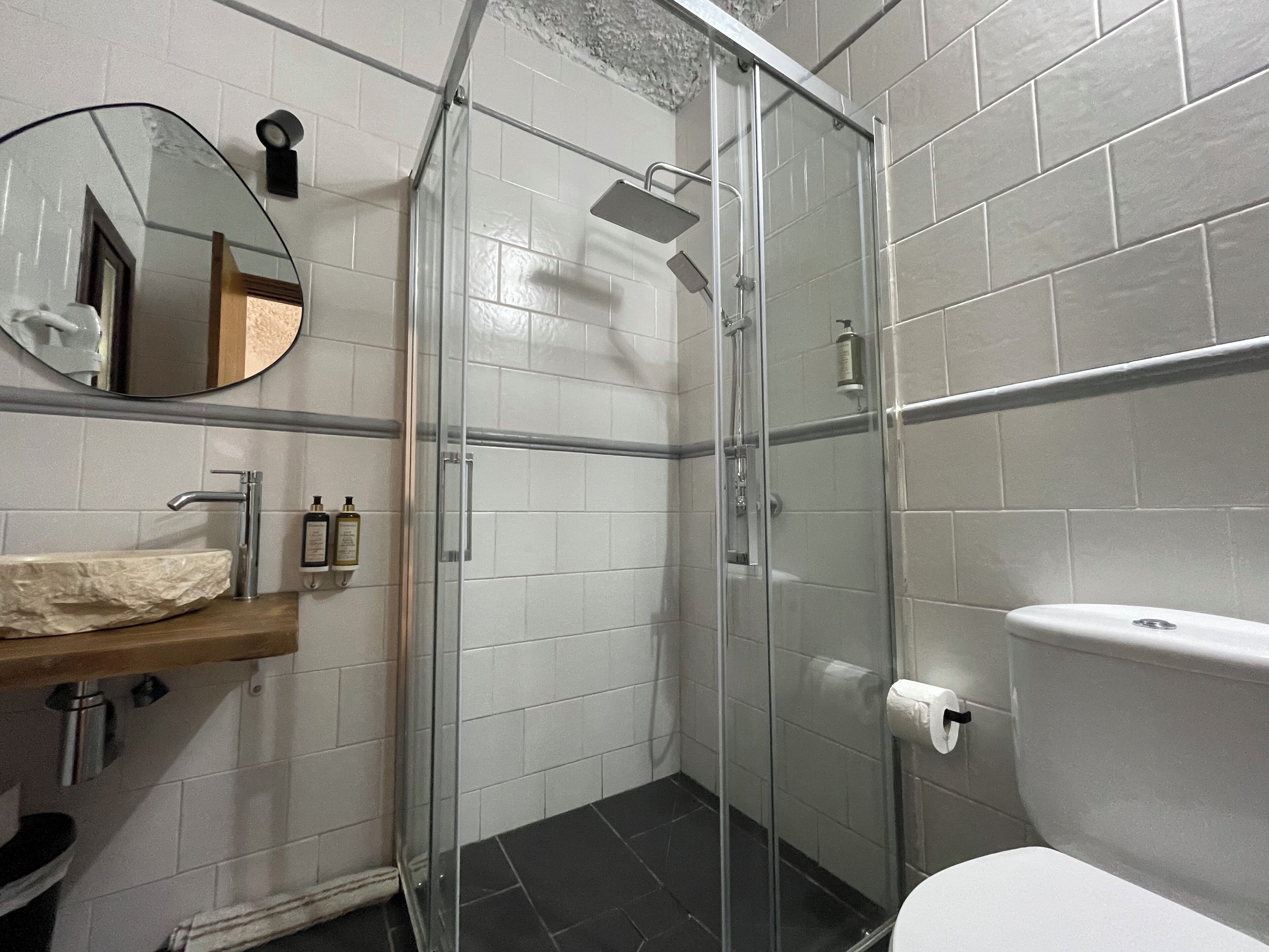 A bathroom with a glass-enclosed shower, a white toilet, a sink with a marble countertop, and a mirror.