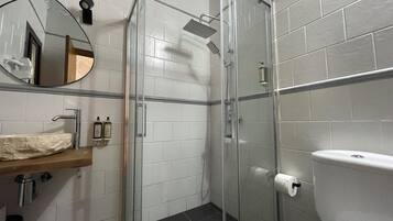 A bathroom with a glass-enclosed shower, a white toilet, a sink with a marble countertop, and a mirror.
