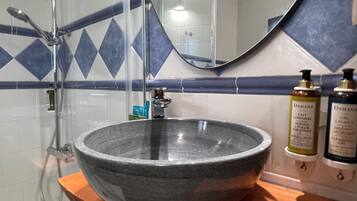 Une salle de bain avec un lavabo en pierre, une douche et deux bouteilles de shampoing.