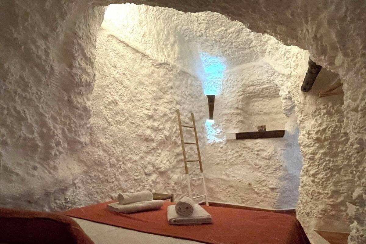 A cozy, cave-like room with a bed, a ladder, and a shelf against the wall.