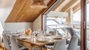 A dining area with a wooden table set for six, a hanging light fixture, and a view of a bridge through large windows. - Åre's best family home (Åre)
