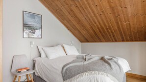 A bedroom with a wooden ceiling, a bed with white bedding, a grey chair, and a framed picture on the wall. - Åre's best family home (Åre)
