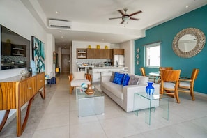 A modern living room with a sofa, coffee table, and chairs, a kitchen with wooden cabinets, and a dining area with a table and chairs.
