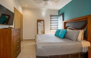 A bedroom with a bed, a wooden dresser, a ceiling fan, and a window with blinds.