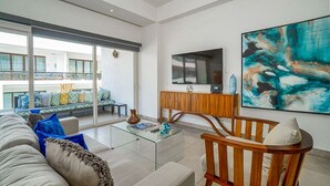 Een moderne woonkamer met een glazen salontafel, een houten stoel en een bank met gestreepte kussens.