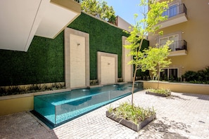 A modern outdoor pool area with a clear pool, a green wall, and a tree.