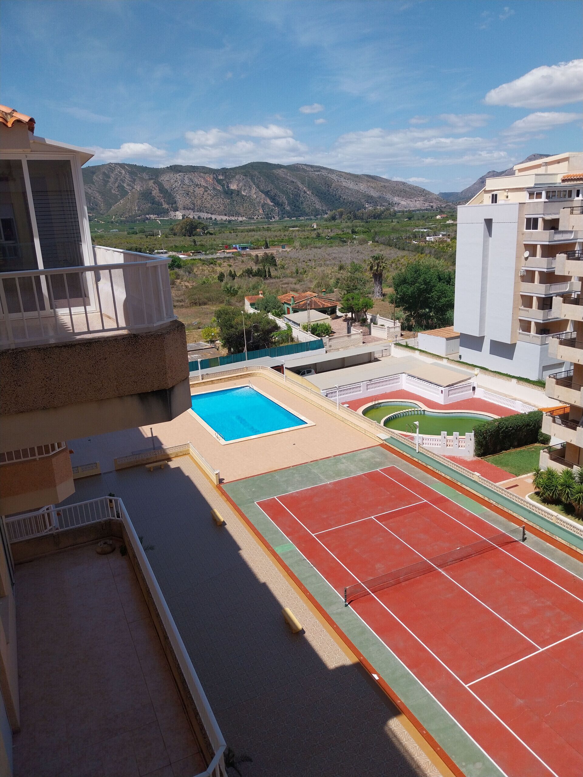 A residential area with a swimming pool, tennis courts, and a view of mountains.