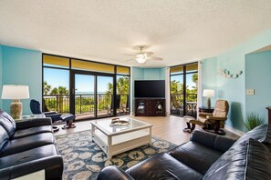 A spacious living room with a large TV, leather sofas, a coffee table, and a balcony with a view. - 🌴🌞Lazy River + Indoor/Outdoor Pools | Oceanfront | South Wind 208 (Myrtle Beach)