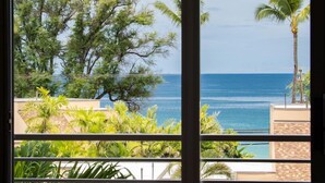 Vista desde un balcón con vista a una playa, palmeras y cielo despejado.