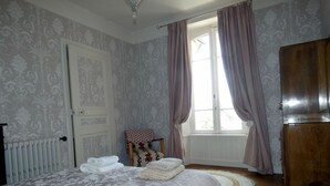 A bedroom with a bed, a chair, a radiator, a window with curtains, and a wardrobe.