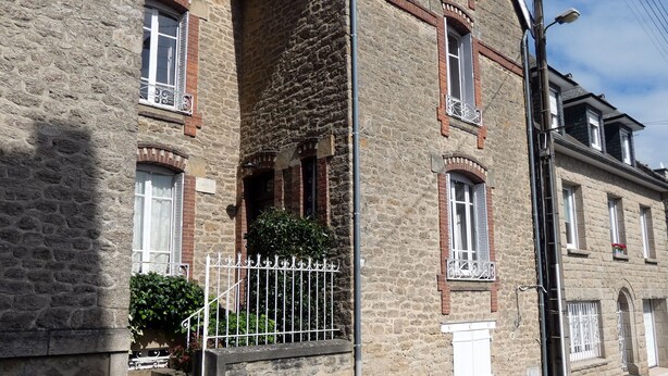 A stone building with a brick facade, multiple windows with shutters, and a metal gate.