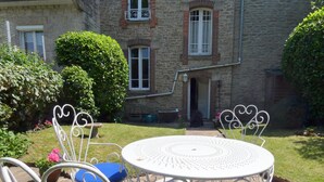 A courtyard with a round table and chairs, surrounded by stone walls and greenery.