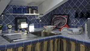 Eine Küche mit Oberlicht, blauen Fliesen, einer Edelstahl-Spüle und einer gefliesten Spritzschutzwand.