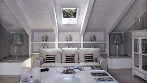 Ein modernes Wohnzimmer mit hohen Decken, einem Oberlicht, einer Sofagarnitur, einem Couchtisch mit Büchern und Dekorationselementen.