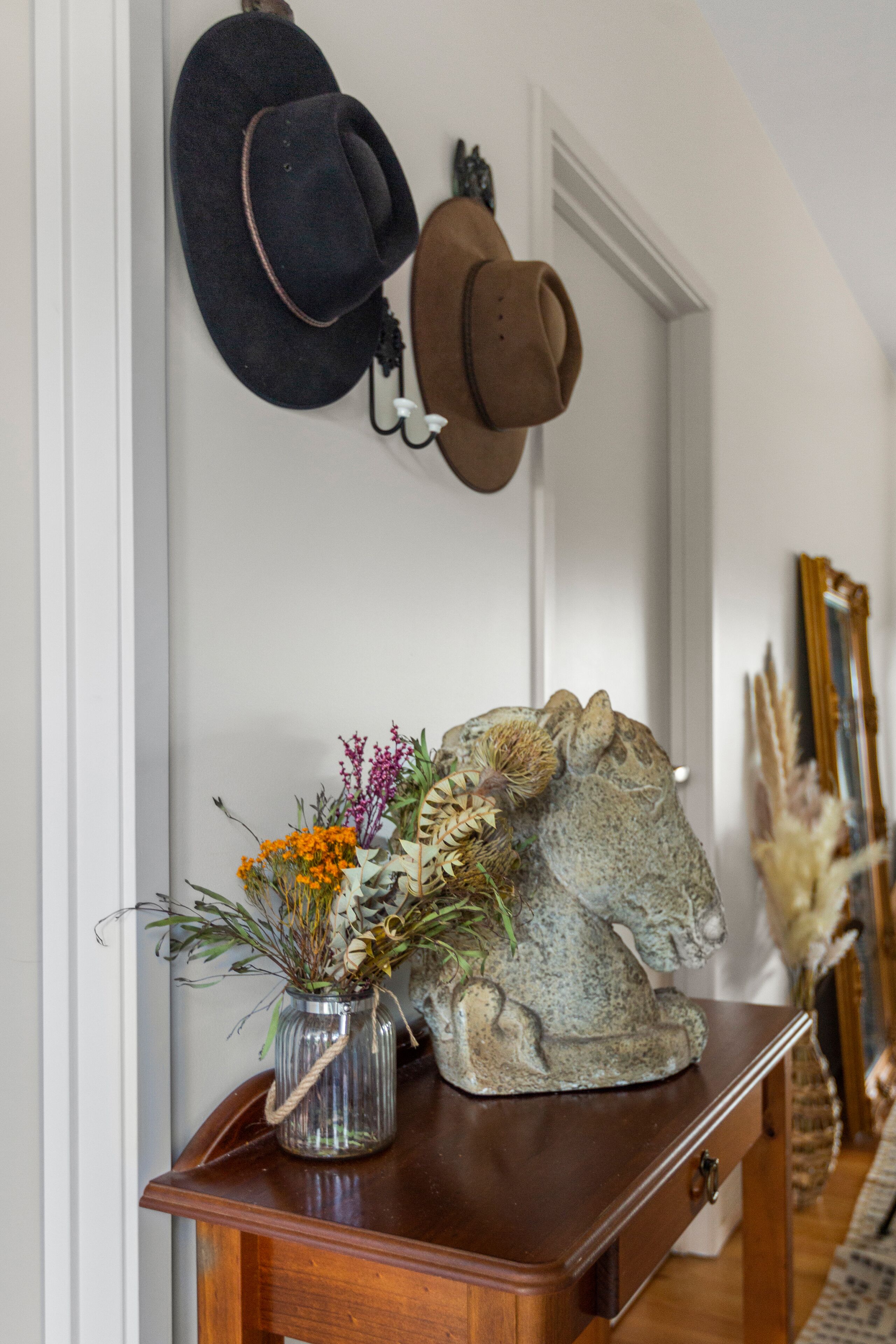 Ein Flur mit einer hölzernen Bank, einer Vase mit Blumen und zwei Hüten an der Wand.