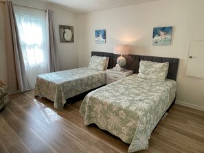 A room with two beds, a nightstand, a lamp, and artwork on the walls.
